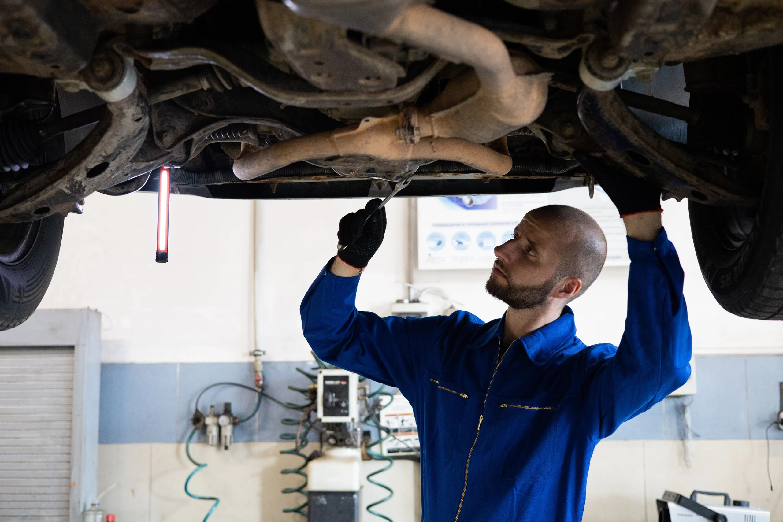 Mechanic inspecting exhaust and engine components underneath a vehicle.