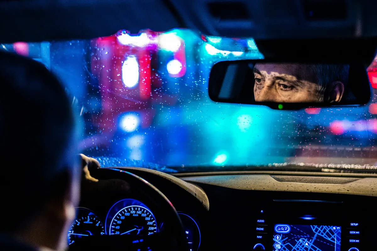Rideshare driver at night, eyes in the rear-view mirror