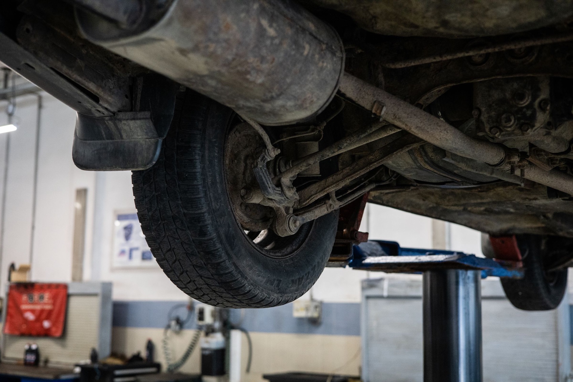 Underside of a car on a two-post lift showing the muffler, exhaust pipe and rear suspension