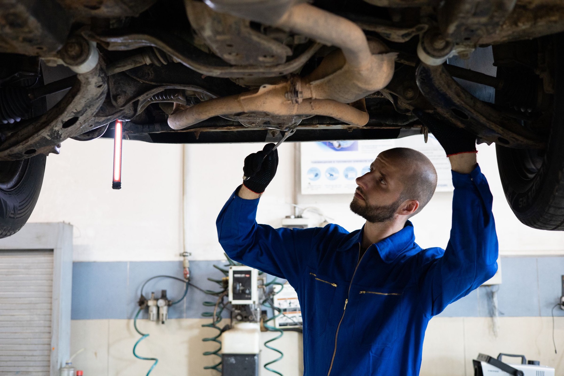 Gloved mechanic checking the exhaust pipe under a car on a lift