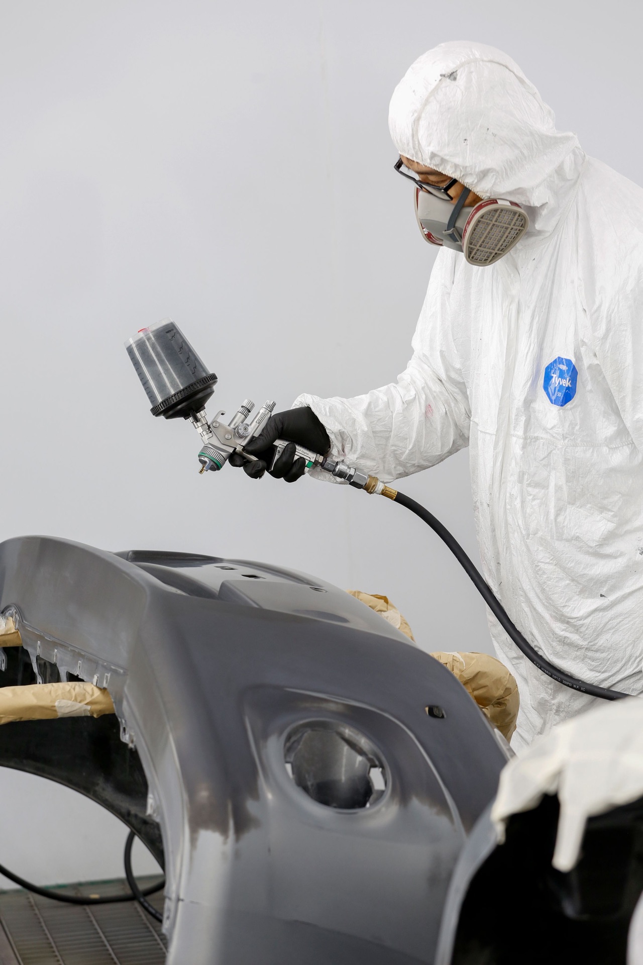 Technician in a protective suit and respirator spraying a protective coating onto a car body panel